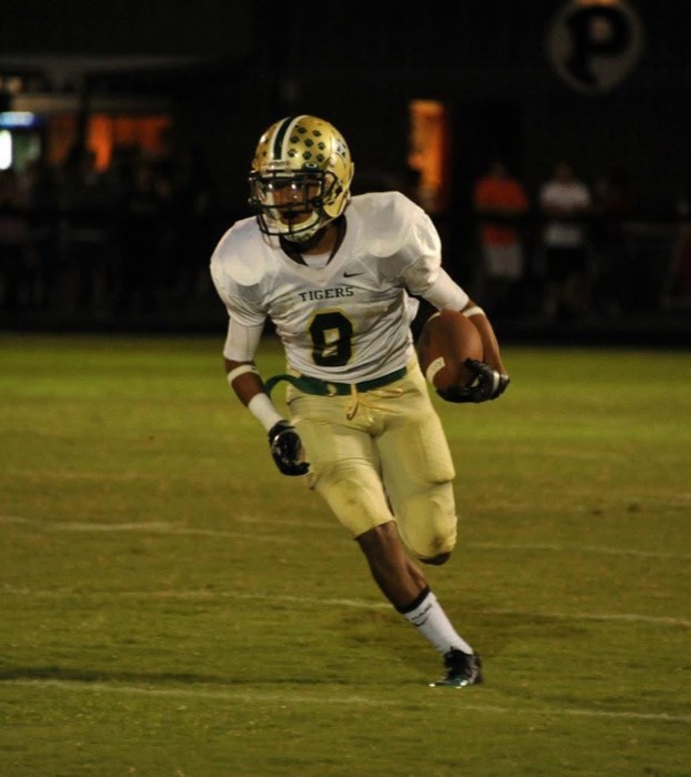 Hiram Velez carrying the ball under the lights in his high school uniform.